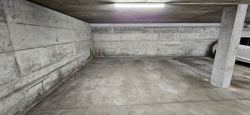 Underground parking garage with concrete walls and floor, ceiling with light, empty parking spots, single car parked