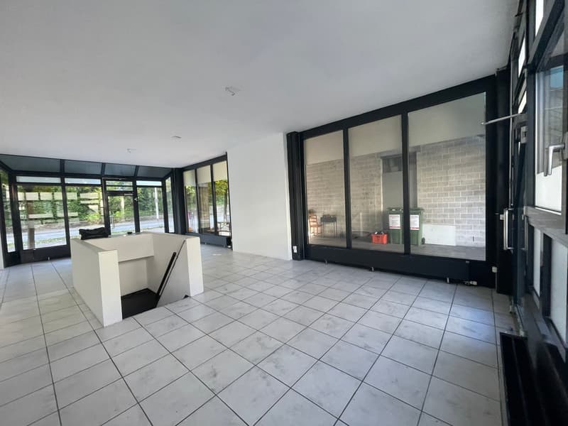 Empty room with white tiled floor, large glass windows, white walls, and a small white desk.