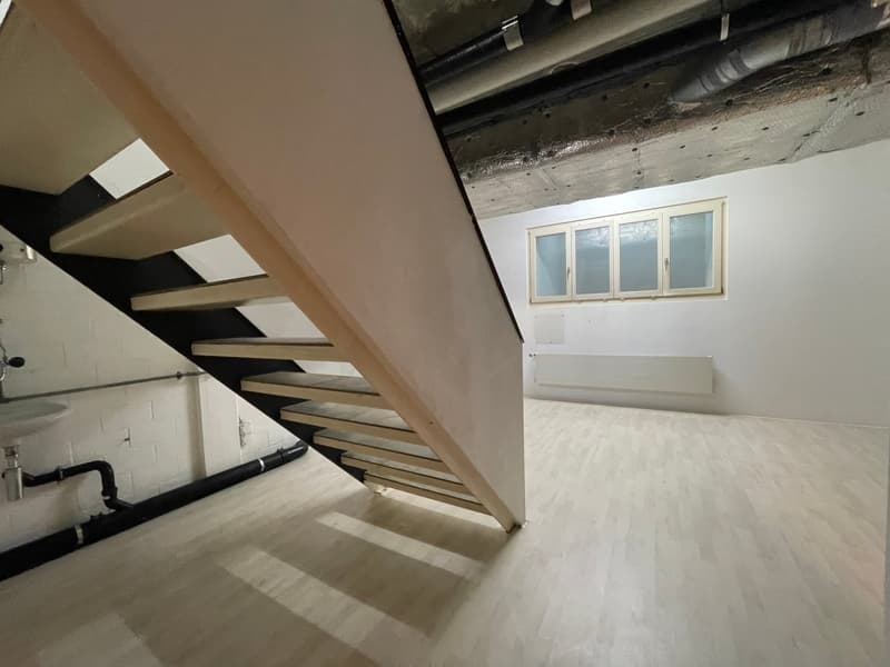 Empty room with wooden stairs, white walls, white floor, window, pipes, and a sink