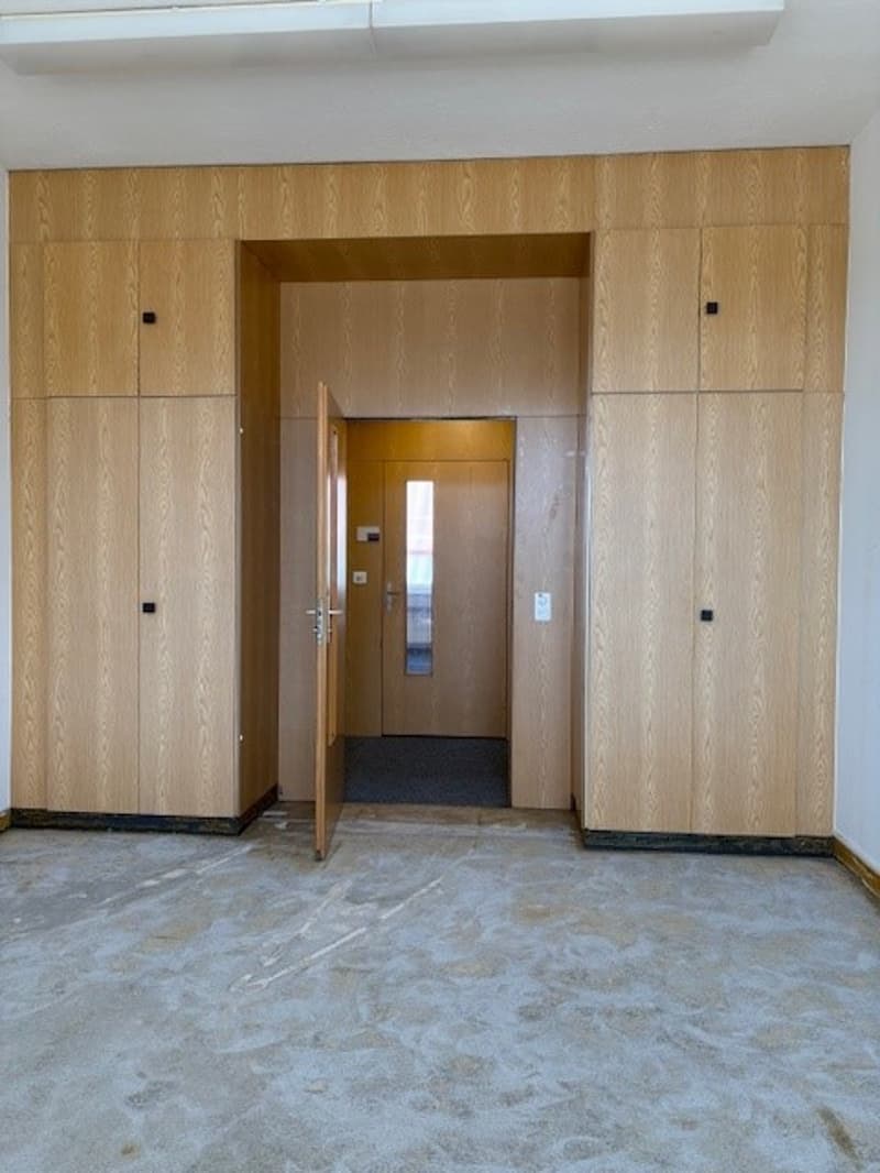 The image shows an entrance hall with wooden paneled walls, a doorway leading to another room, and a tiled floor.