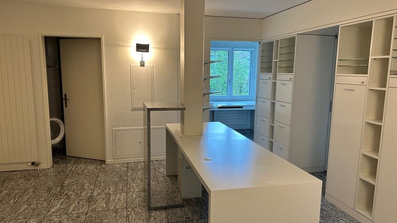 Spacious kitchen with granite countertops, built-in shelving units, and a dishwasher. Large window providing natural light. Tiled flooring throughout the room.