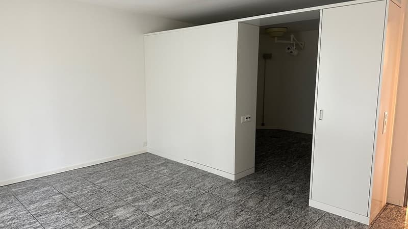 Empty room with white walls, gray tile flooring, and built-in cabinets or closets along one wall.