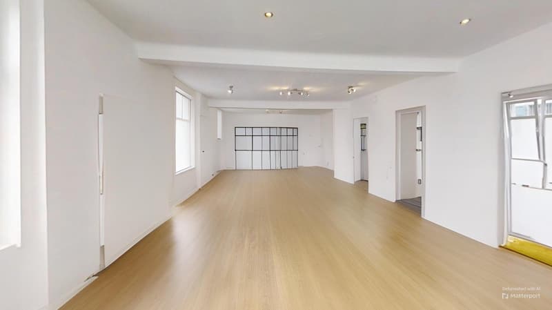 Large open space with white walls, hardwood flooring, and recessed lighting. The room appears to be an empty studio or office space with a grid-like wall feature.