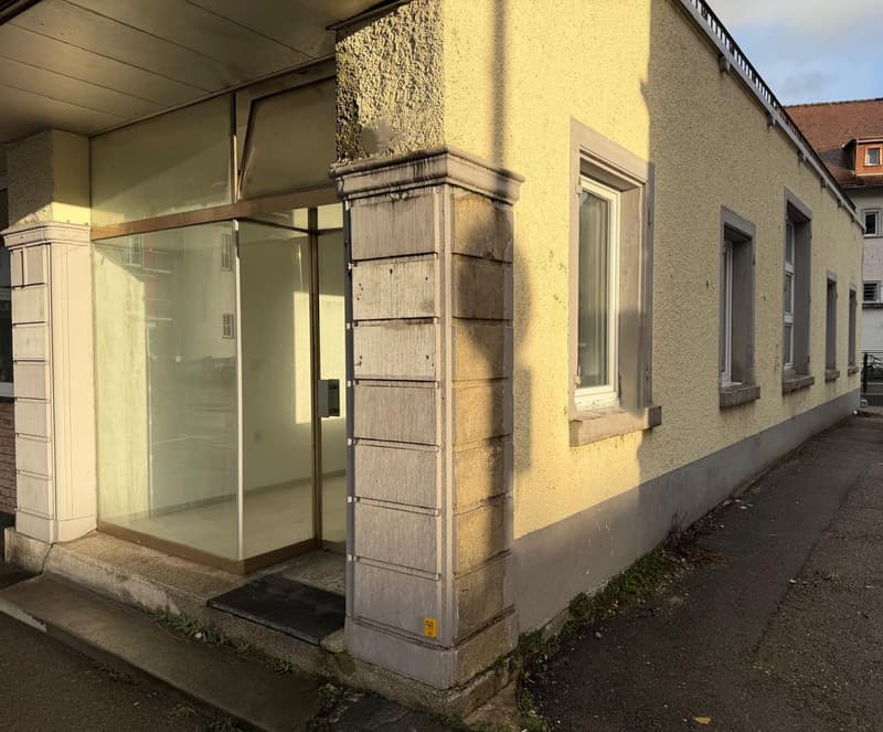 Commercial building with glass door and windows, yellow painted walls, concrete steps leading up to the entrance