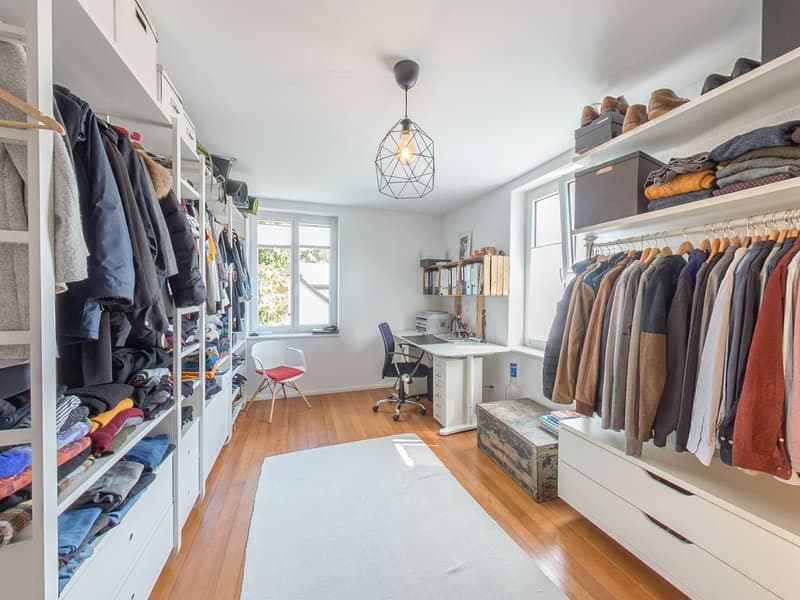 walk-in closet with white shelves, wooden floor, white rug, desk, chair, office chair, books, printer, lamp, windows