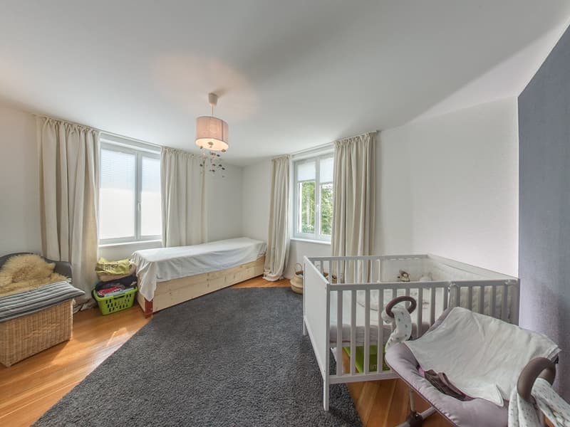 A nursery with a crib, a small bed, a basket, a rug, and a lamp
