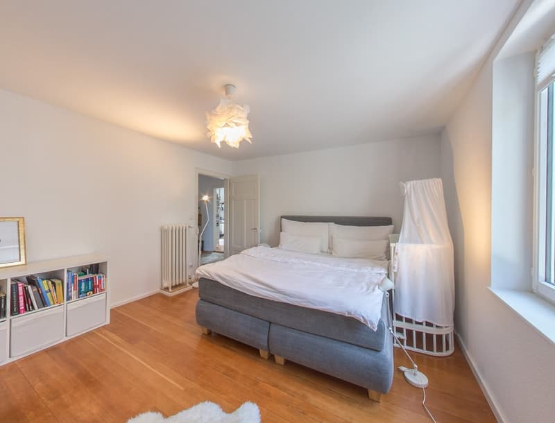 bedroom with bed, lamp, radiator, books, rug, window