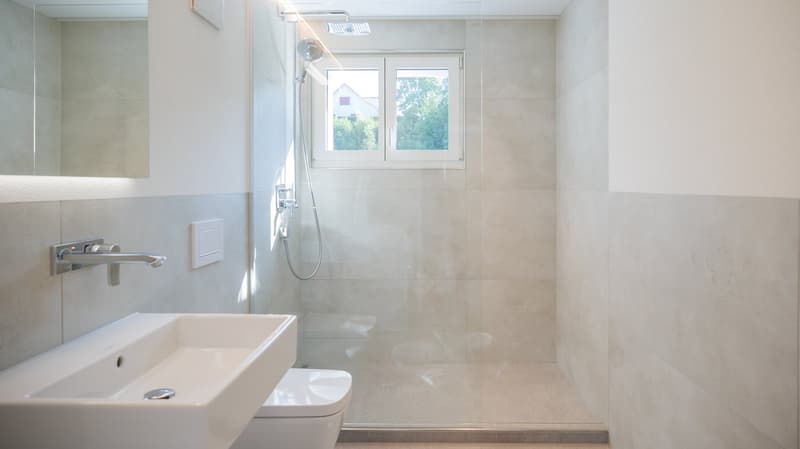 modern bathroom with white tiles, glass shower enclosure, white sink, white toilet, mirror, shower head, faucet
