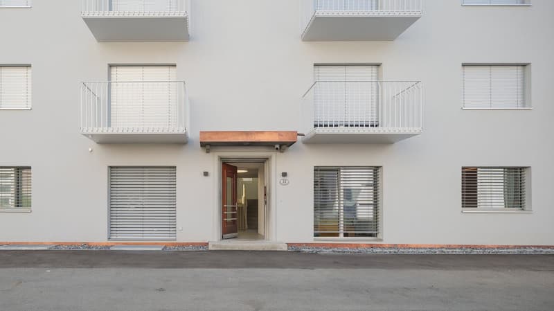 Modern white building, multiple balconies, glass windows, entrance door, number 12