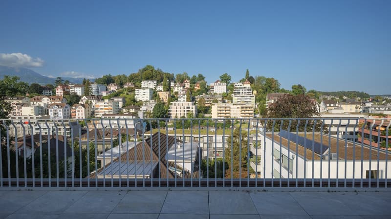 Balcony with metal railing, overlooking a cityscape with various buildings, trees, and mountains in the distance