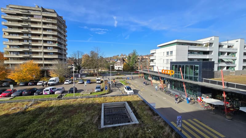 Multi-story building, parking lot, trees, storefront, bicycles, and vehicles.