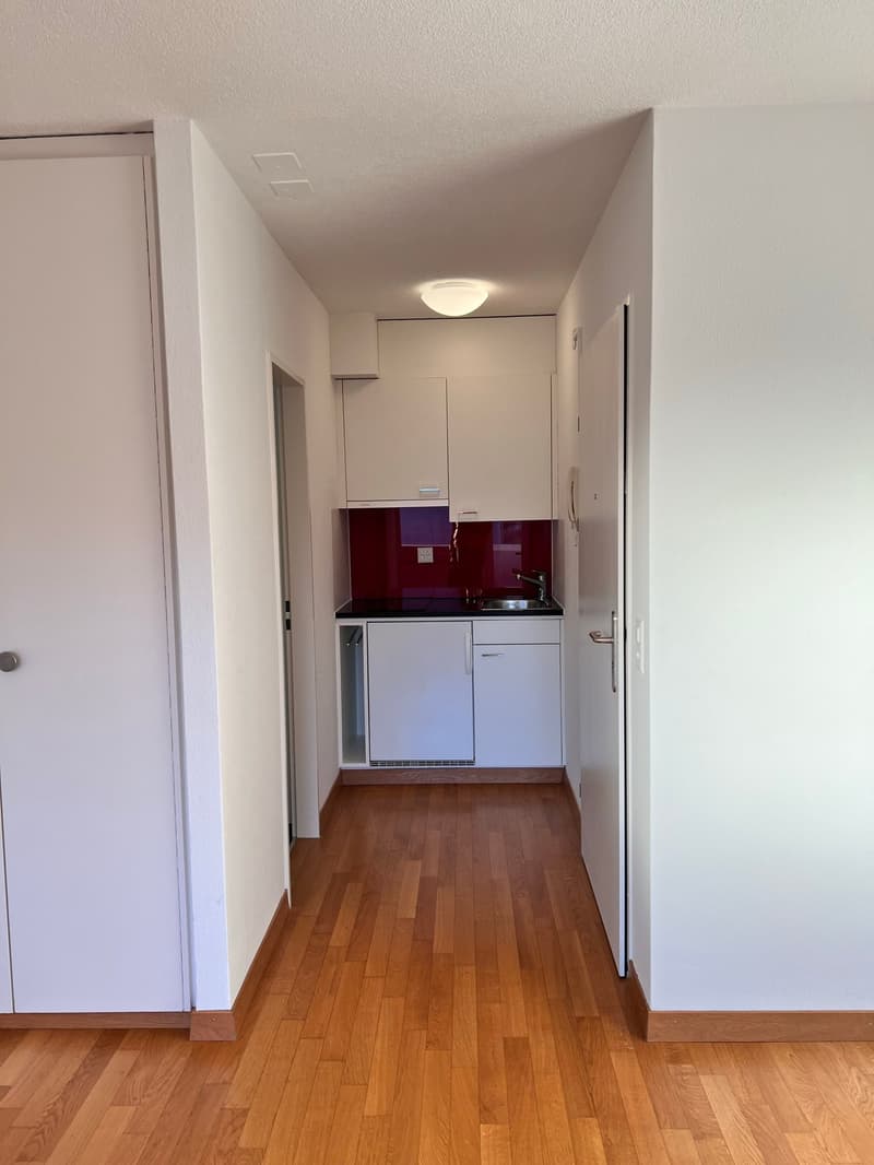 Empty kitchen with white cabinets, wooden floor, sink, faucet, and a small window