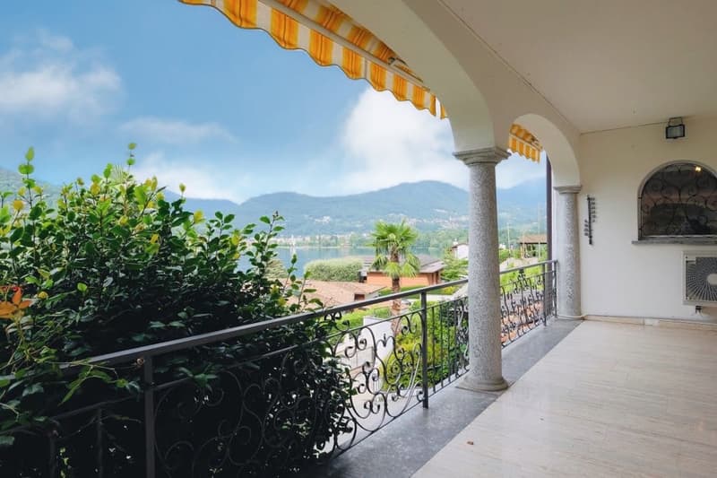 Covered balcony with ornate wrought-iron railing, overlooking a scenic view of mountains and a body of water
