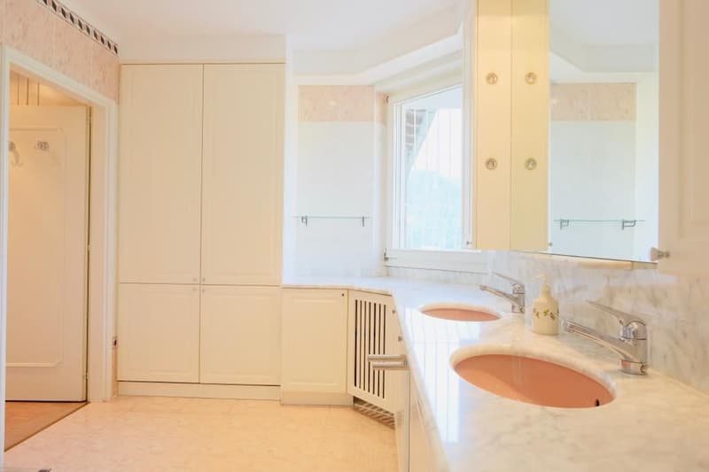Spacious bathroom with white walls, marble countertops, double sinks, and a private washing machine