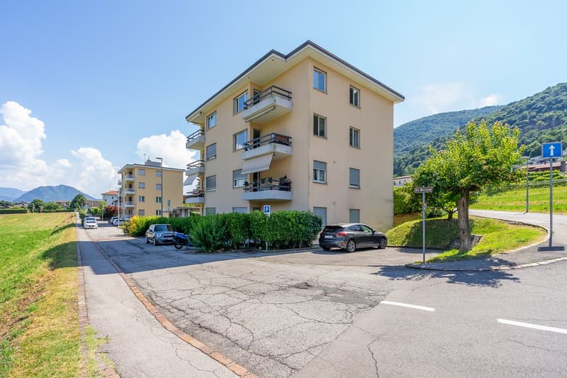 3-story apartment building with yellow exterior, balconies, and parking spaces in front