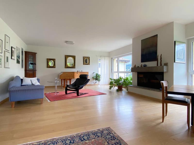 Spacious living room with hardwood floors, large windows, a fireplace, a blue sofa, a wooden piano, and various framed artwork on the walls.