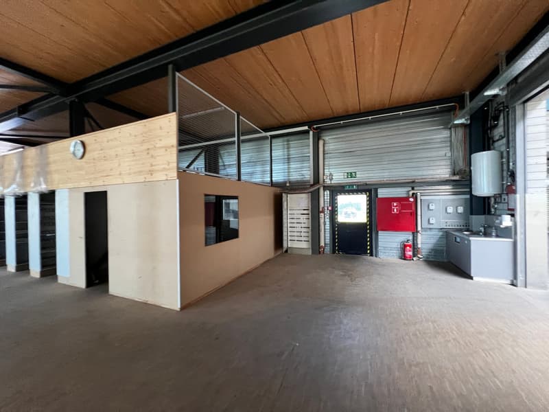 Industrial building with metal beams, wooden ceiling, concrete floor, small office, fire extinguisher, sink, and a clock