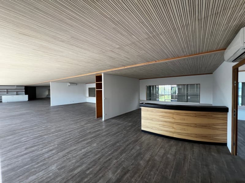 large open space, wooden floor, wooden reception desk, white walls, glass windows, air conditioners