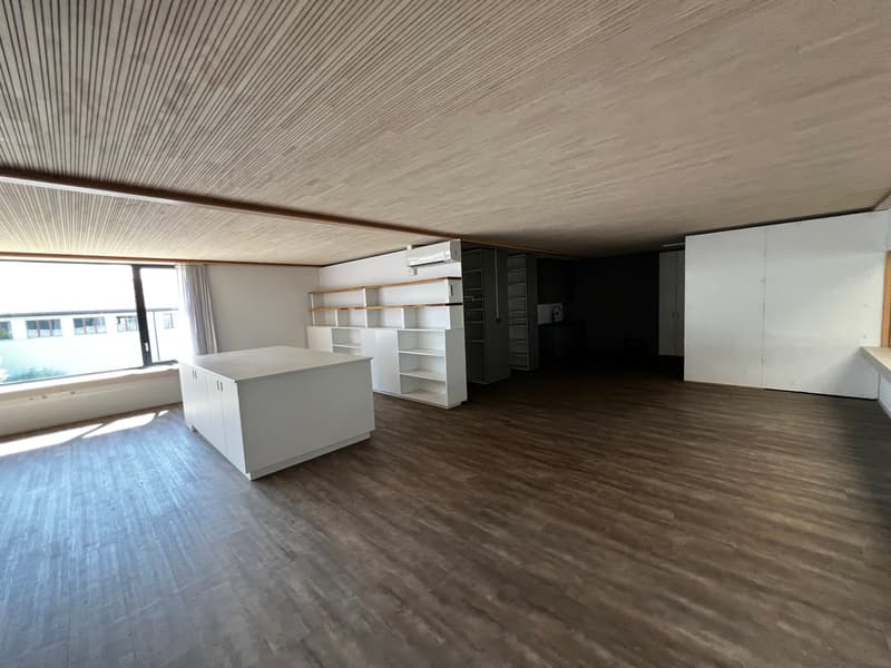 Empty room with wooden floor, white walls, large window, white kitchen island, white shelves, and a ceiling with wooden beams.