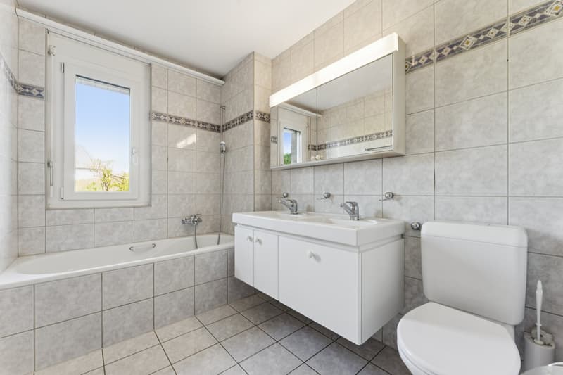 Das helle Badezimmer überzeugt mit einer Badewanne und einem grosszügigen Doppellavabo
