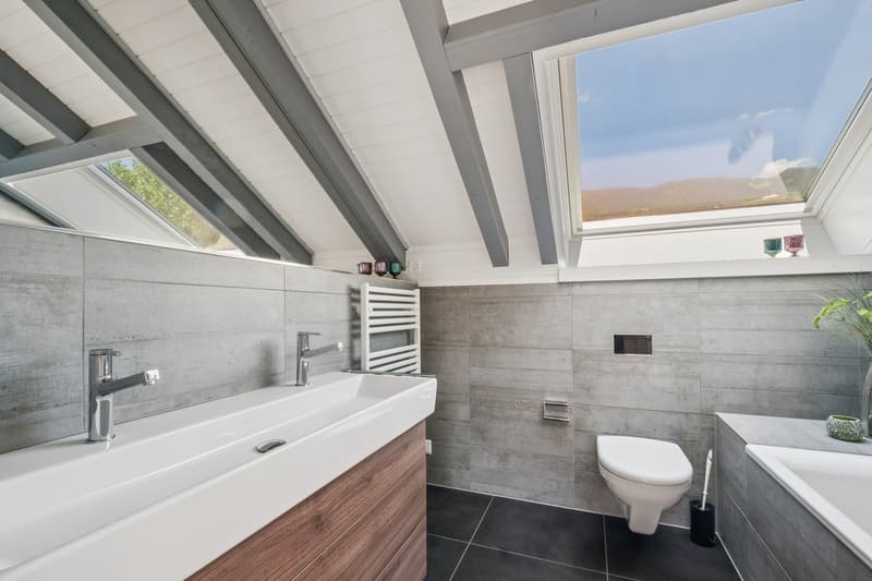 Im Obergeschoss befindet sich ein stilvolles, modernes Badezimmer mit Badewanne und Doppel-Lavabo