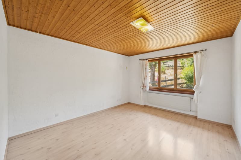 Das geräumige Schlafzimmer mit viel Platz, einer warmen Holzdecke und einer ruhigen Aussicht ins Grüne