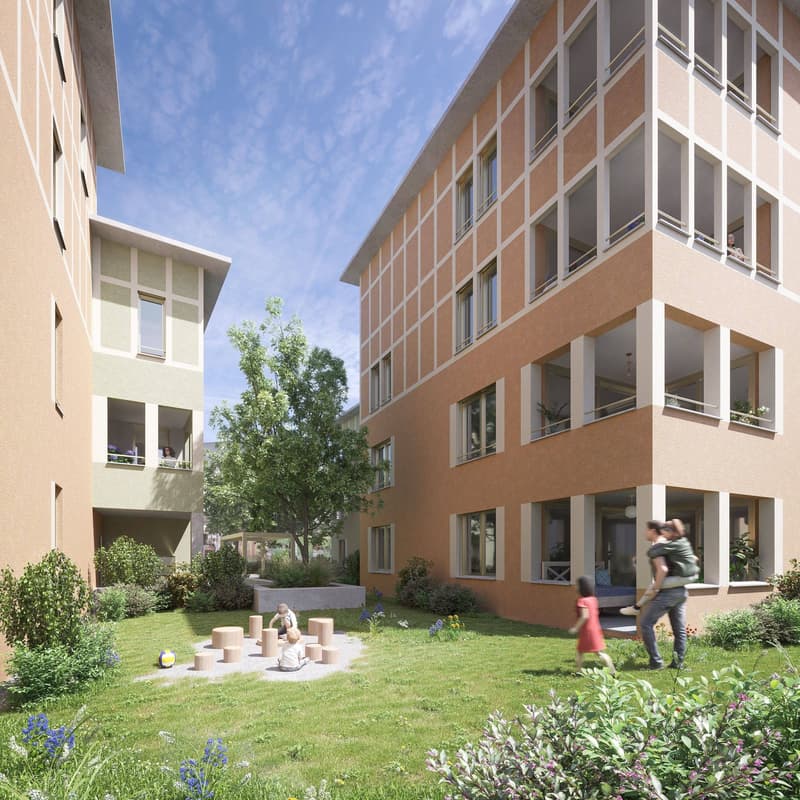 Multi-story apartment building with brick and glass facade, surrounded by a landscaped courtyard with grass, trees, and a children's play area.