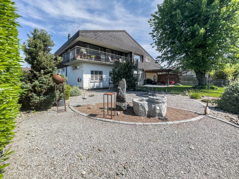 2-story house with a slanted roof, gray brick exterior, balcony, garage, and a landscaped yard with gravel, rocks, and plants