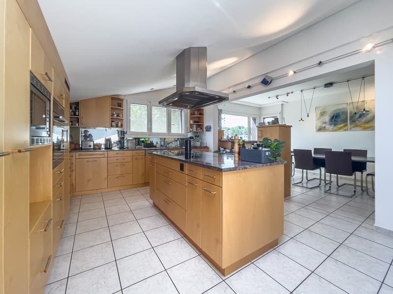 Modern kitchen with wooden cabinets, granite countertop, kitchen island with stove and microwave, stainless steel extractor, under cabinet lighting, dining table with chairs, white tiled floor