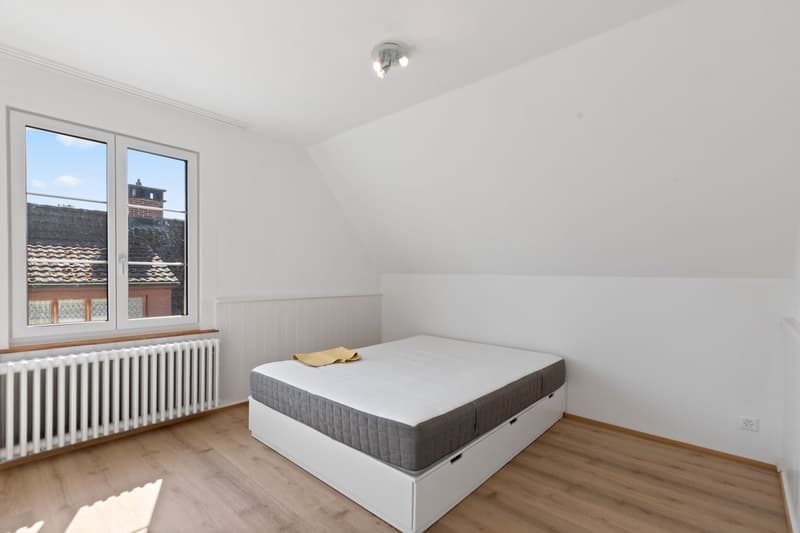 white walls, wooden floor, single bed with mattress, window, radiator, ceiling light