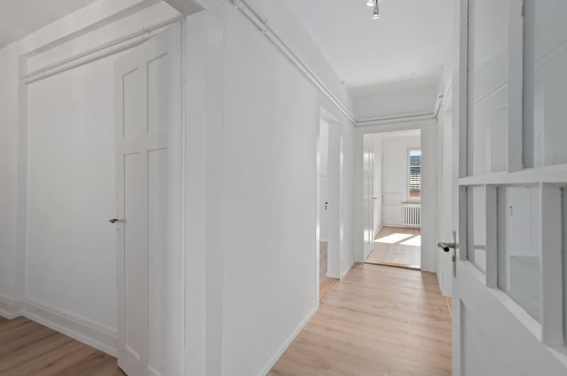 Empty hallway with white walls, wooden floor, glass doors, and a window with a view.