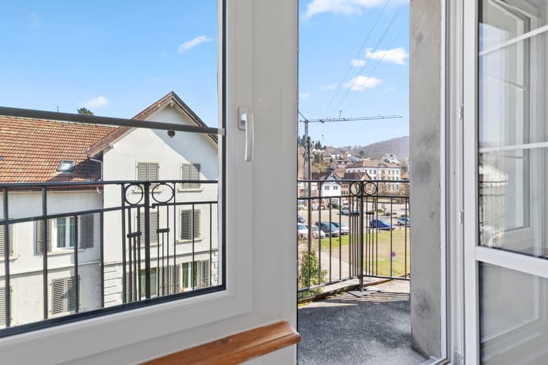 Open door leading to balcony, metal railing, view of street and houses