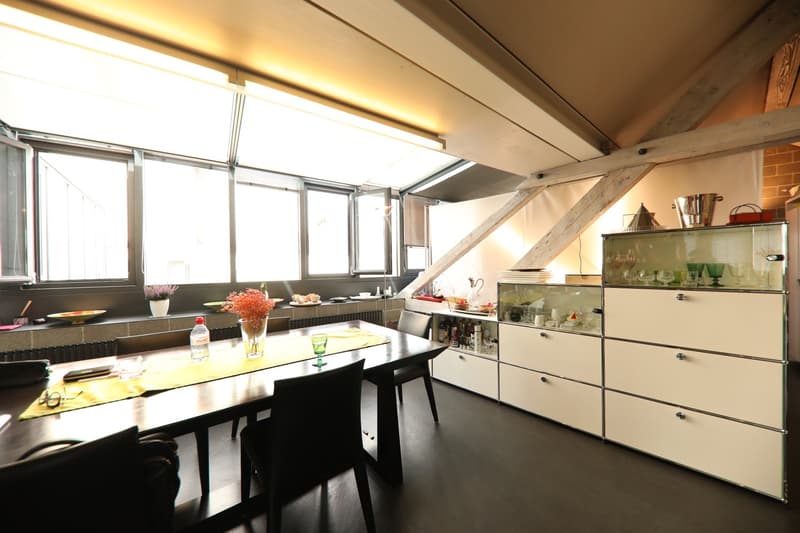 dining area with long table, chairs, cabinets, wine glasses, vase with flowers, windows