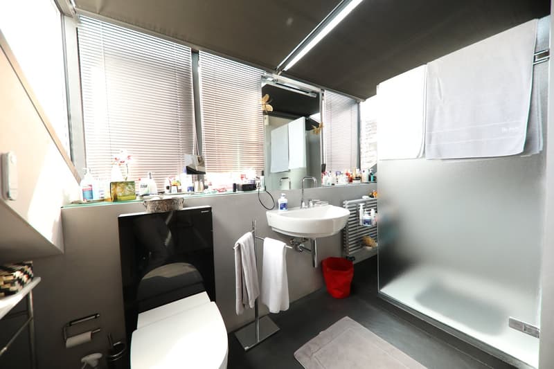 modern bathroom, black tiled shower wall, white toilet, white sink, two towel racks, floor-mounted towel rack, small shelf with items
