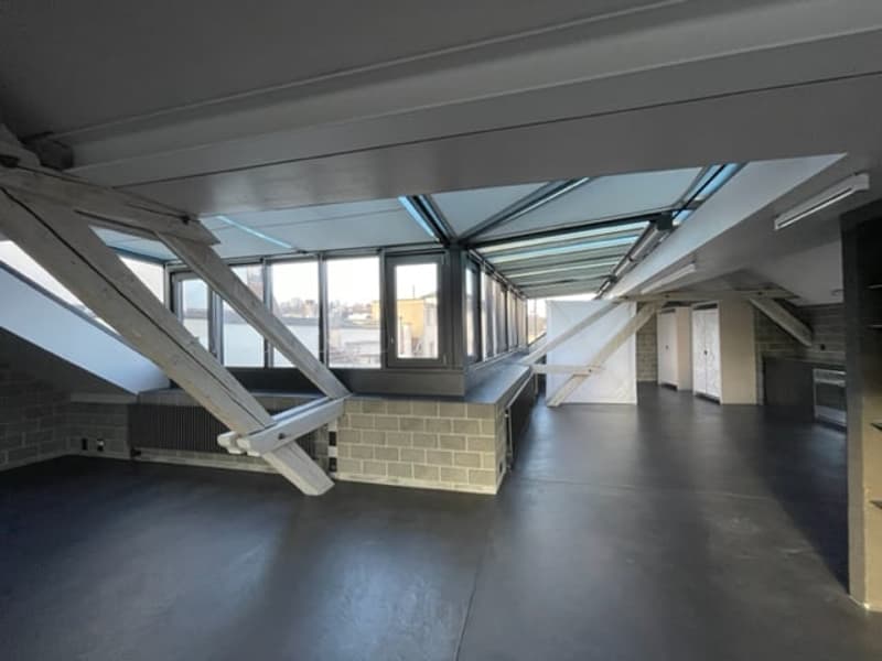 a room with gray flooring, large windows, wooden beams and glass skylight