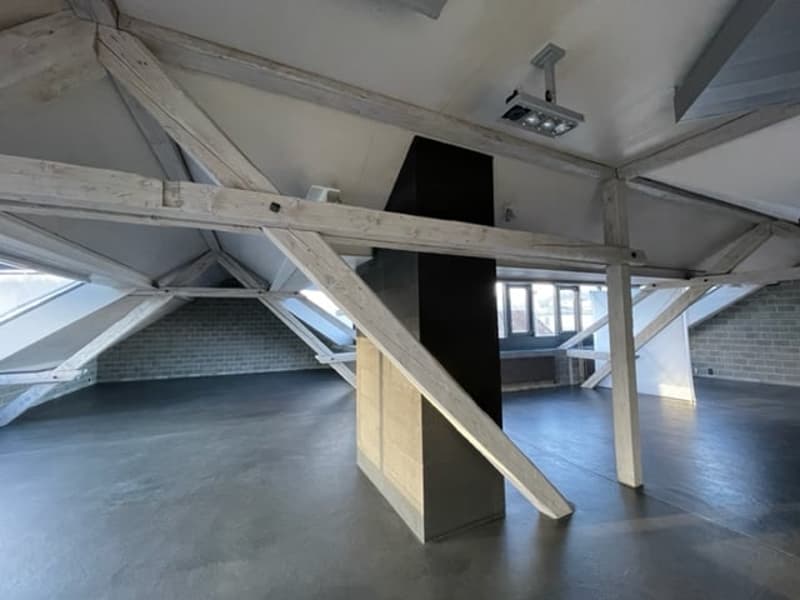 spacious attic room, exposed wooden beams, concrete floor, windows, central support column
