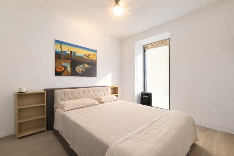 bedroom with bed, bedside table, shelf, ceiling fan, large window with balcony