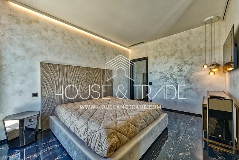 Luxury bed with quilt, patterned headboard, marble floor, textured walls, nightstand with drawer, large mirror, ceiling pendants, open doorway