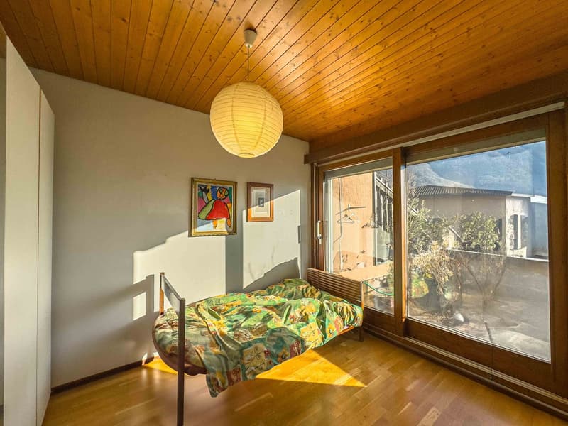 single bed, wooden floor, white walls, large windows, wooden ceiling, lamp, paintings