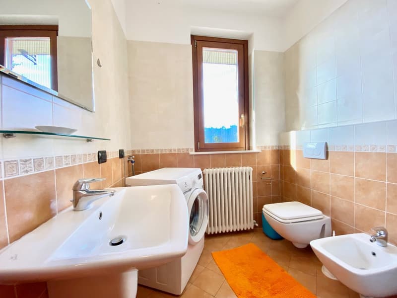Bathroom: sink, white tiled wall, washing machine, window, toilet, bidet, mirror, radiator, rug