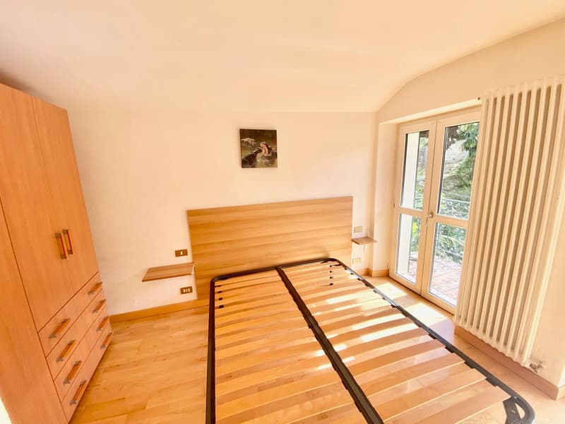 Spacious bedroom with wooden flooring, a wooden headboard, built-in wardrobes, and a sliding glass door leading to a balcony or terrace.