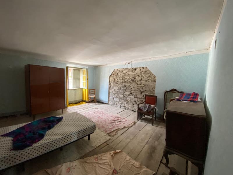 Empty room with old wooden floor, blue wall, wooden bed, wooden cabinet, chair, stone wall, and small window
