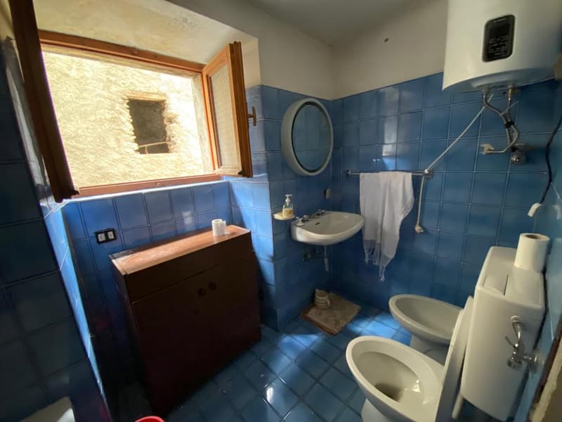 Bathroom with blue tiles, wooden cabinet, sink, toilet, mirror, and window.