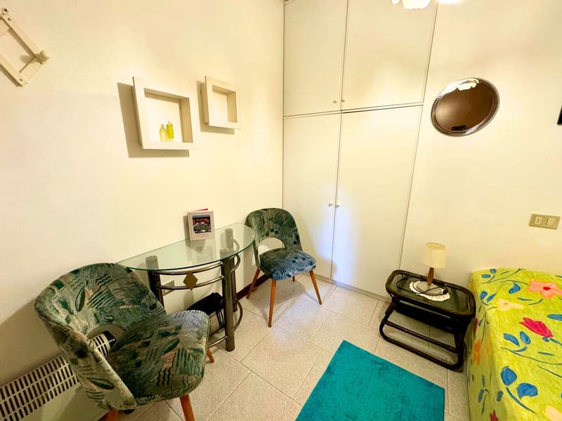 minimalist room with table, chairs, night stand, mirror, shelves, radiator, and a small bed with flowers
