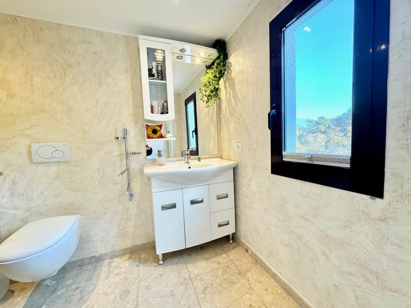 Spacious bathroom with marble-like walls, a white vanity cabinet with drawers, a sink, and a large window providing a scenic view outside.