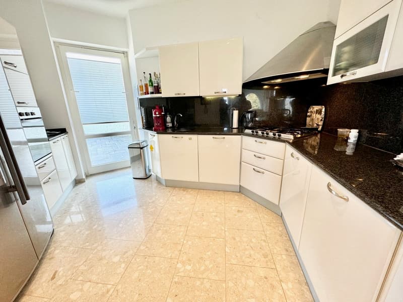 Spacious kitchen with white cabinets, black granite countertops, stainless steel appliances including a dishwasher and washing machine, tiled flooring, and a large window providing natural light.
