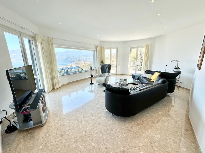 Spacious living room with large windows offering a scenic view, hardwood flooring, black leather sofas, coffee table, and a balcony or terrace area