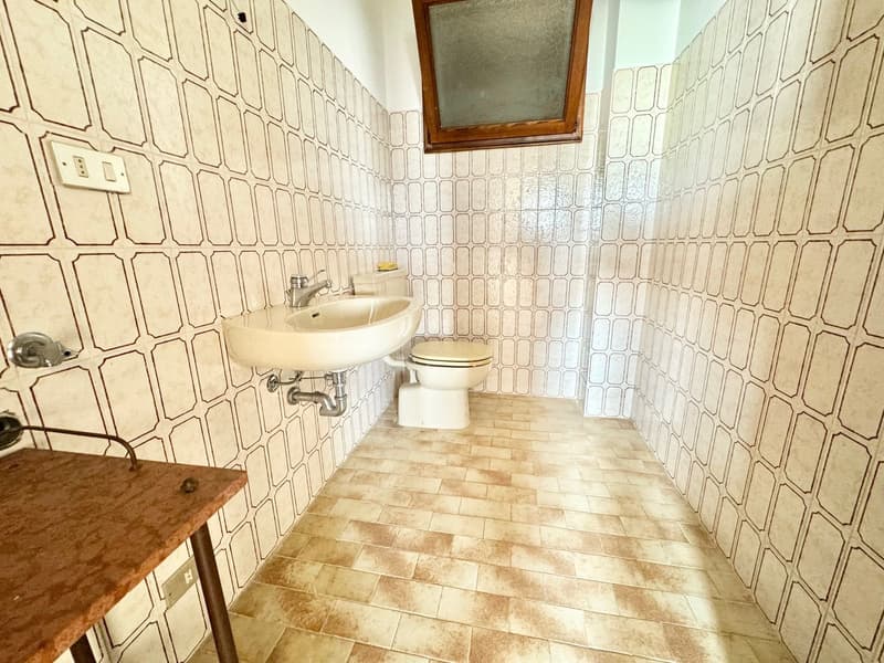 modern bathroom with a sink, toilet, small shelf, tiled walls and floor, a window
