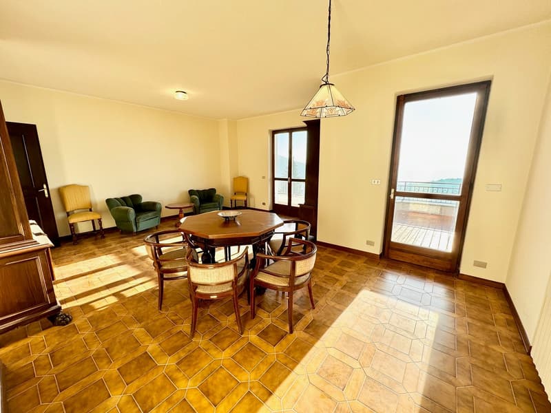 Dining room with a round wooden table and chairs, wooden flooring, wooden door, glass doors leading to balcony with railings, bright and sunny