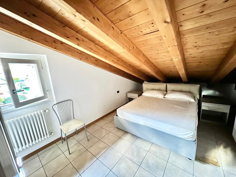 Attic bedroom with wooden ceiling beams, tile flooring, large window, and a double bed with bedside tables